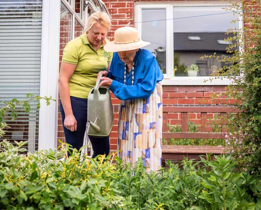 Carer helping a lady water plants in her garden at home